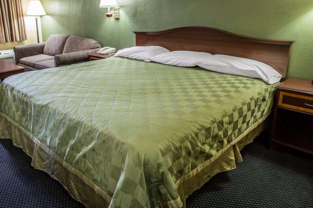 A hotel room with a large bed, a chair, a bedside table, a lamp, and a painting on the wall.