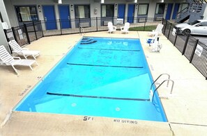 A swimming pool with no diving allowed, surrounded by lounge chairs and a building with blue doors.