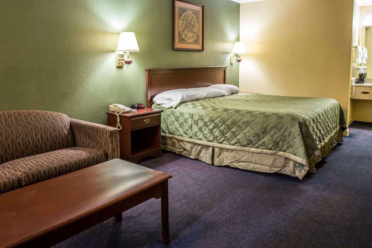 Ein Hotelzimmer mit Bett, Stuhl, Nachttisch mit Telefon und Lampe.