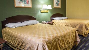 Une chambre d’hôtel avec deux lits, une table de chevet avec une lampe et deux tableaux encadrés au mur.