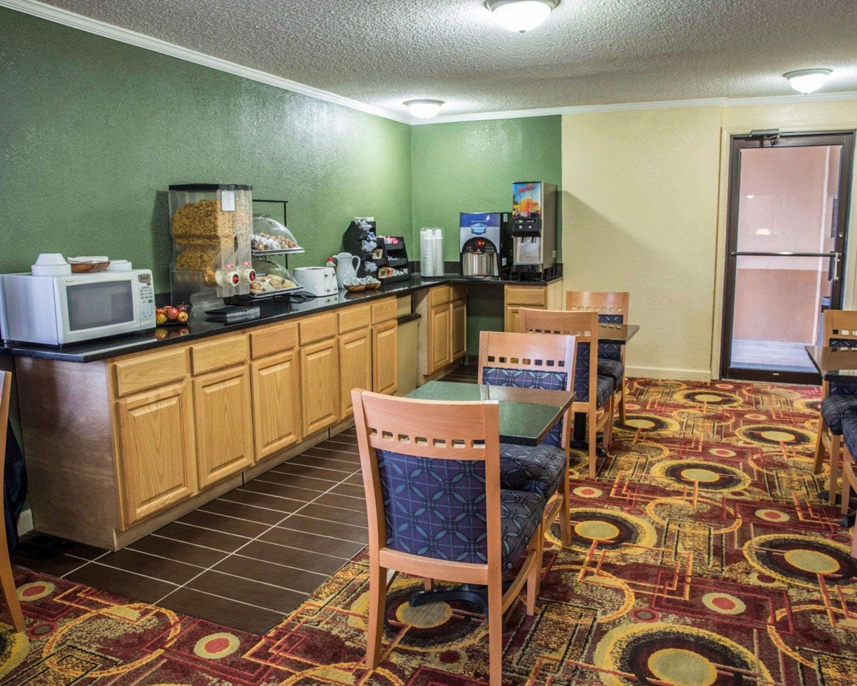 A compact hotel kitchen with wooden cabinets, a microwave, a coffee maker, and a buffet station.