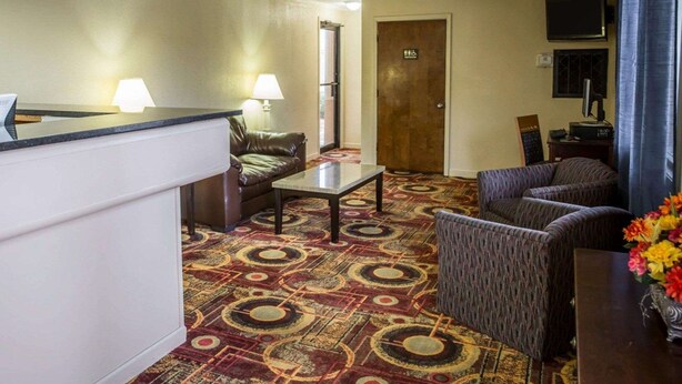 A hotel lobby with a reception desk, a sofa, a chair, a small table, and a television. - Rodeway Inn & Suites Plymouth Hwy 64 (Plymouth)