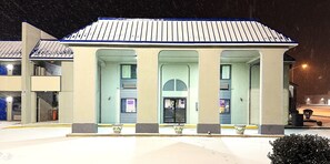 A building with a light-colored facade and a blue roof. It has three large arched openings, likely entrances or windows, and a small entrance area with a door.