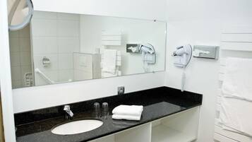 Une salle de bain d’hôtel avec un lavabo au comptoir noir, un miroir, un sèche-cheveux et un porte-serviettes.