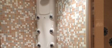 A shower with multiple nozzles and a control panel, set against a tiled wall with a checkered pattern.