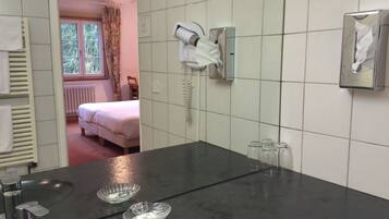 Ein Hotelbad mit einem großen Spiegel, einem Föhn, einem Telefon und einem Waschbecken mit zwei Glasbechern.