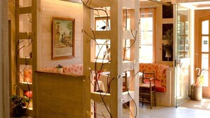 A reception area with a wooden reception desk, a framed painting, and a seating area with chairs and a table. - Auberge d'Imsthal (La Petite-Pierre)
