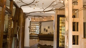 A lobby with a tree-like light installation on the ceiling, a reception desk, and a bar area with shelves of bottles. - Auberge d'Imsthal (La Petite-Pierre)