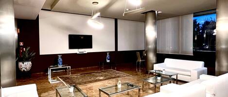 A modern living room with white sofas, glass coffee tables, and a flat-screen TV mounted on the wall.