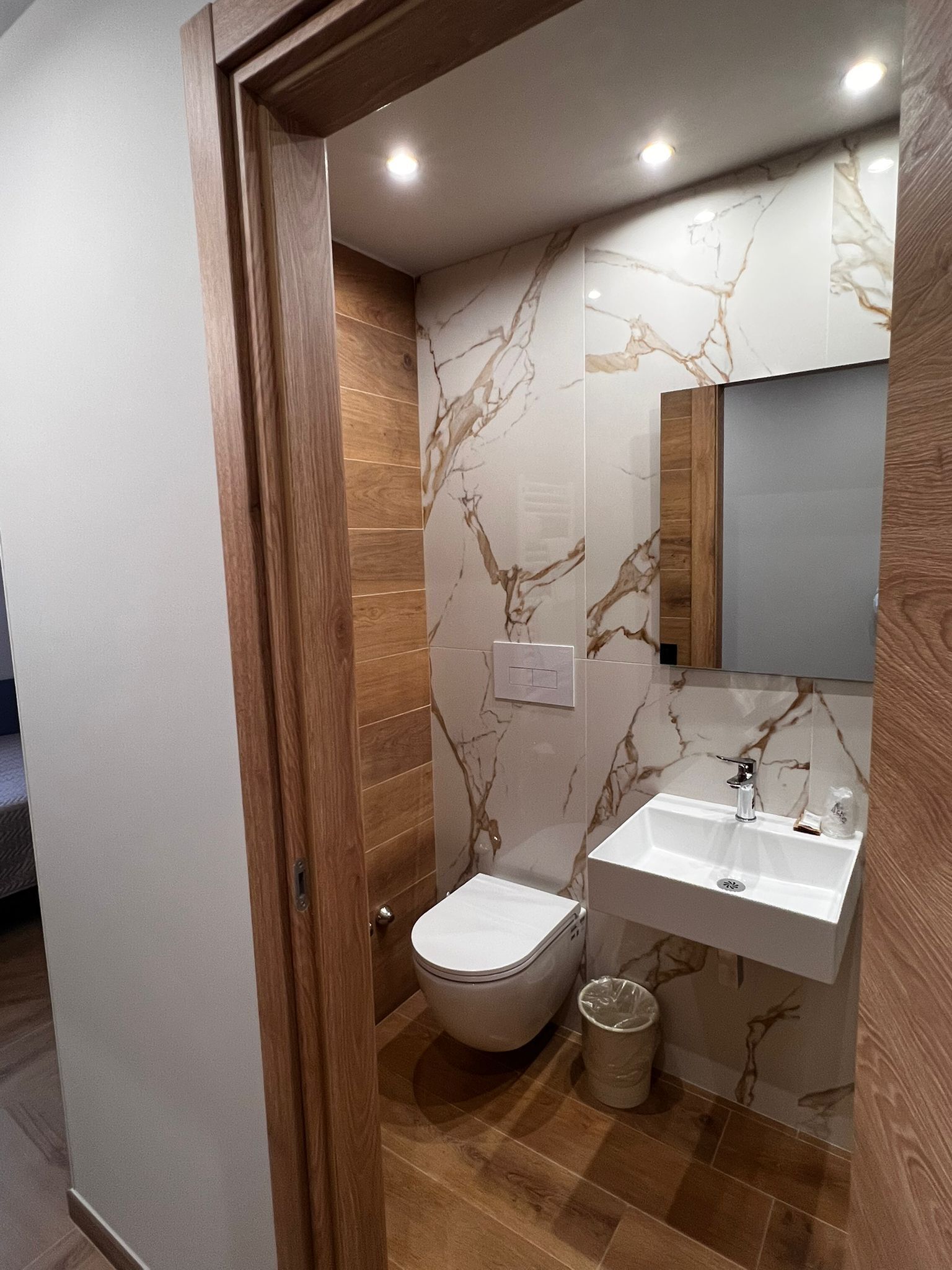 Une salle de bain avec une porte en bois, des toilettes, un lavabo et un miroir.
