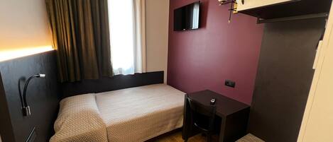 A hotel room with a bed, a desk, a TV, and a wardrobe.