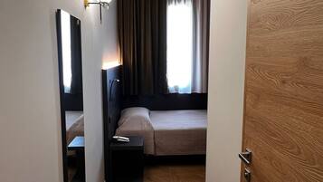 Een hotelkamer met een bed, nachtkastje, lamp, spiegel en een houten deur.