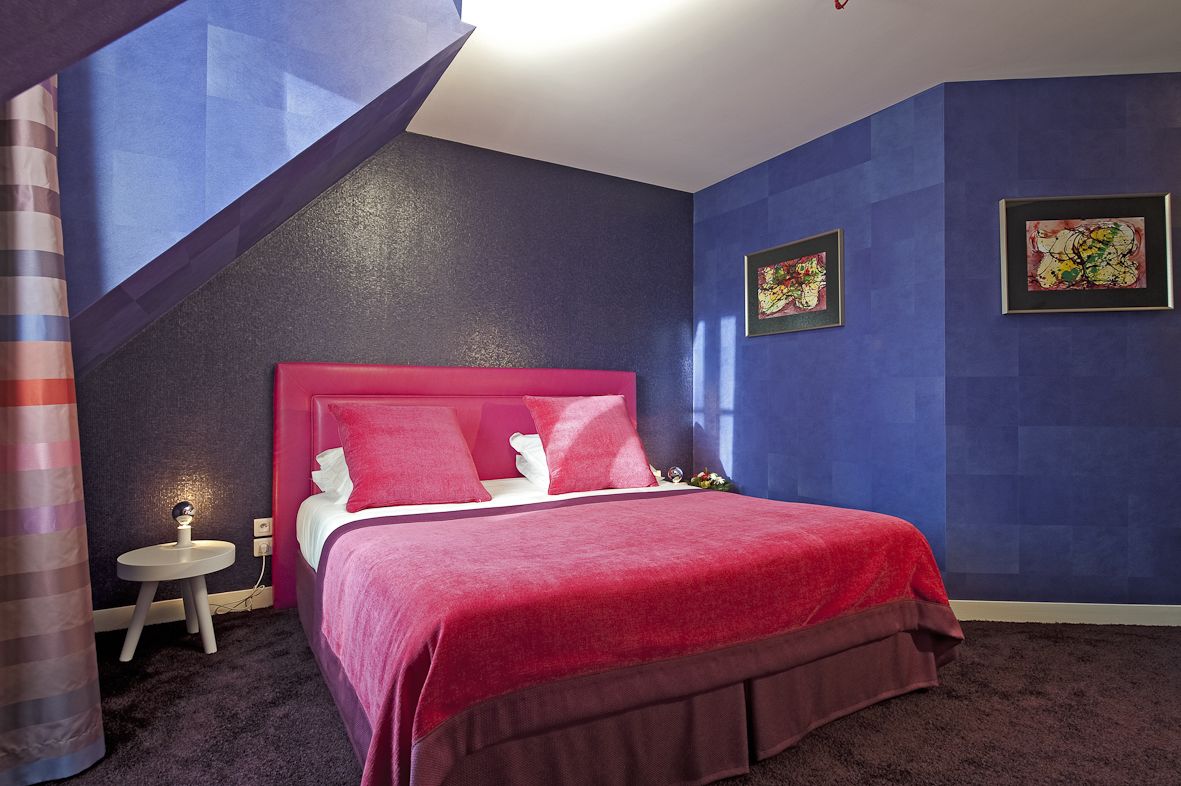 Ein Schlafzimmer mit einem roten Bett, einem kleinen Nachttisch und zwei gerahmten Kunstwerken an der Wand.