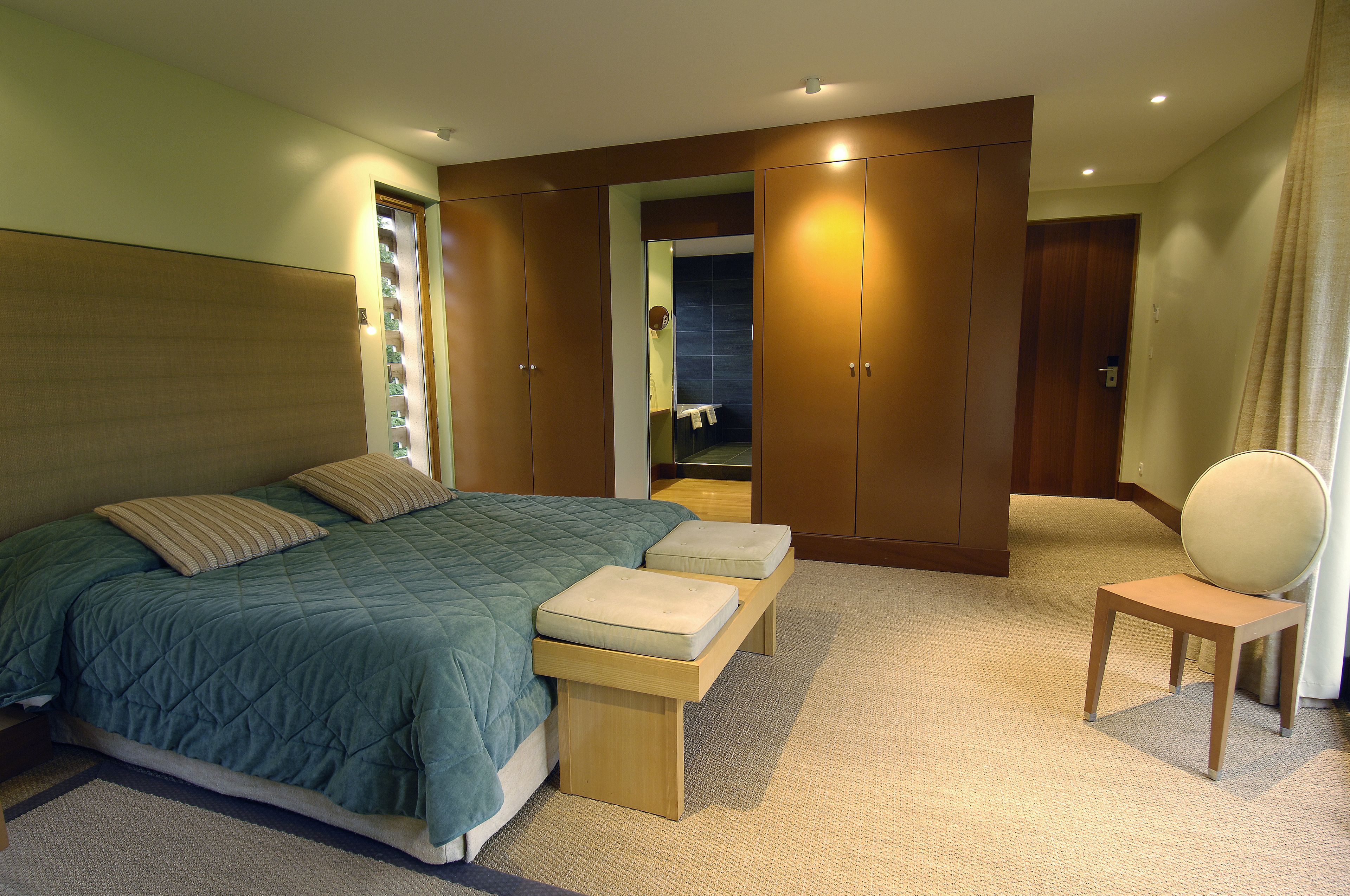 Un dormitorio con cama, banco, silla y armario.