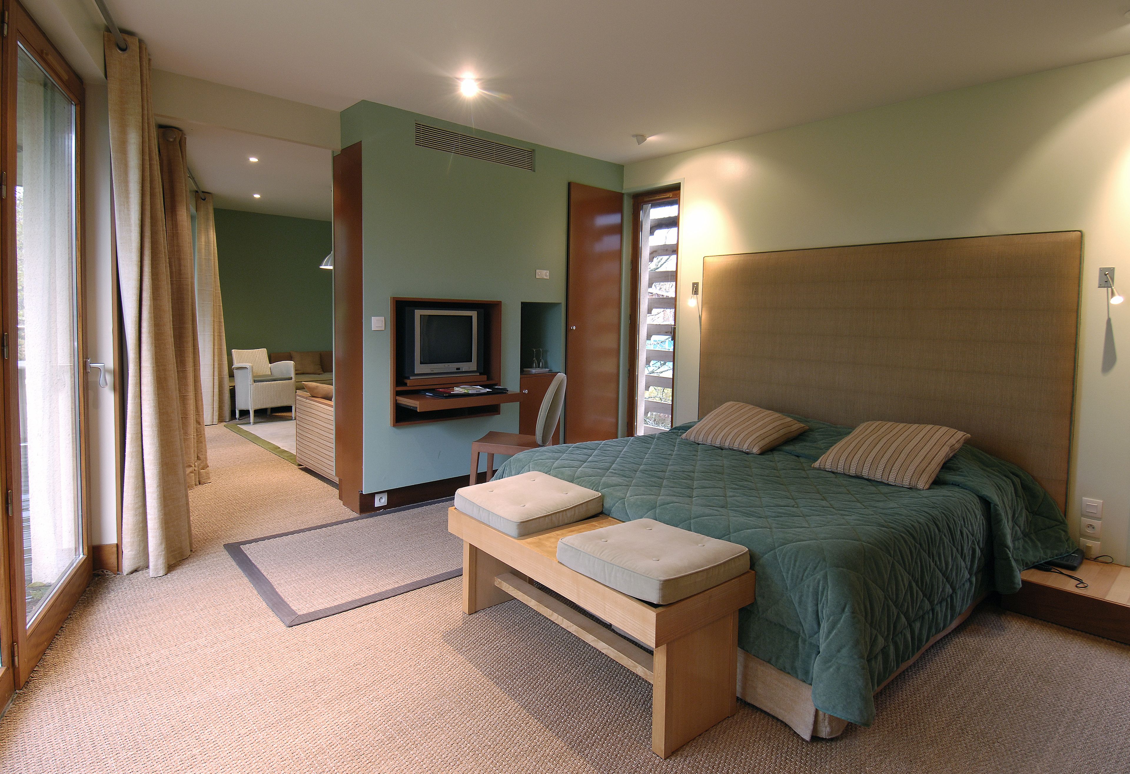 A bedroom with a large bed, a bench, a television, and a desk.