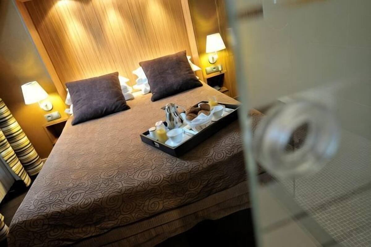 Een hotelkamer met een bed, twee kussens, nachtlampjes en een dienblad met spullen op het bed.
