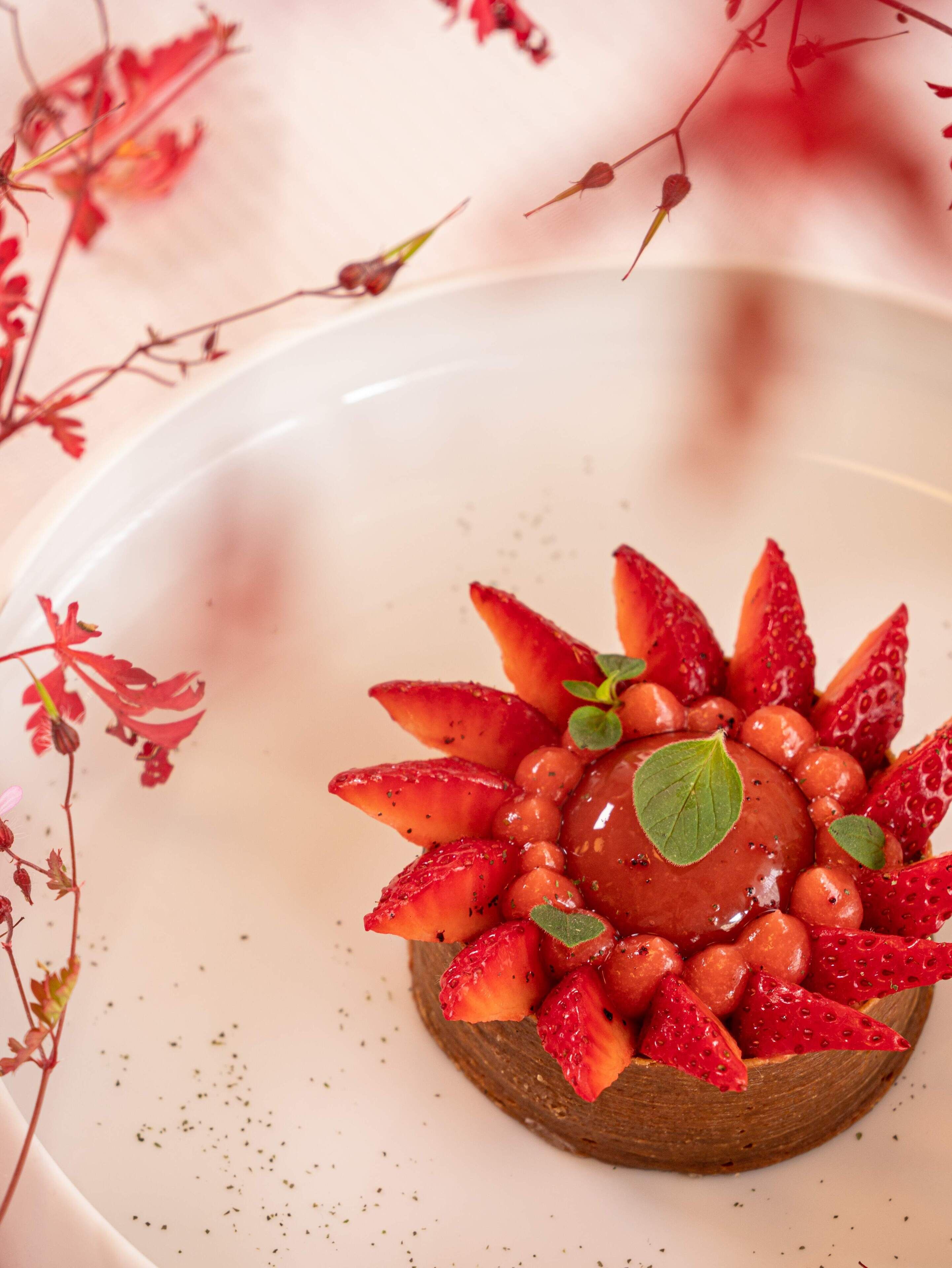 Un postre sobre un plato blanco, con fresas y una baya en el centro.