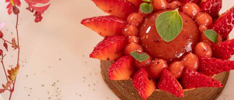 Un postre sobre un plato blanco, con fresas y una baya en el centro.