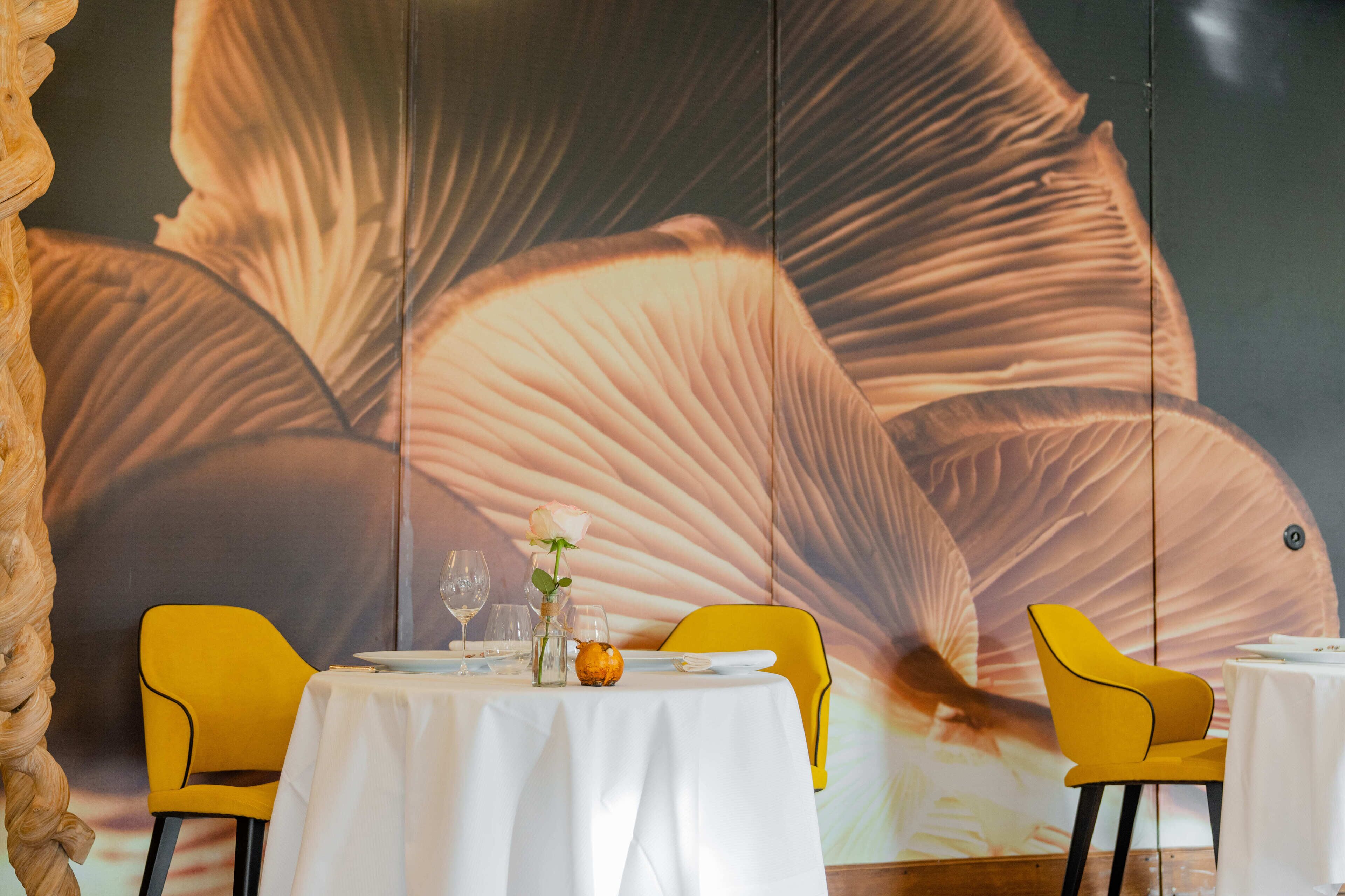 A dining area with a table set for two, yellow chairs, and a large wall mural.