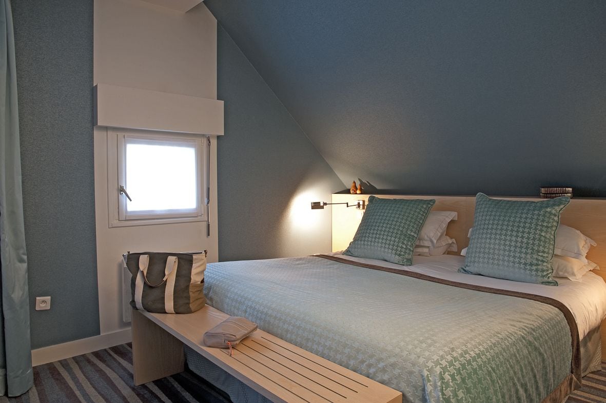 A bedroom with a bed, a bench, a window, and a nightstand.