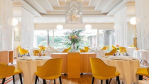Un espace repas avec des tables rondes, des chaises jaunes et une composition florale au centre.