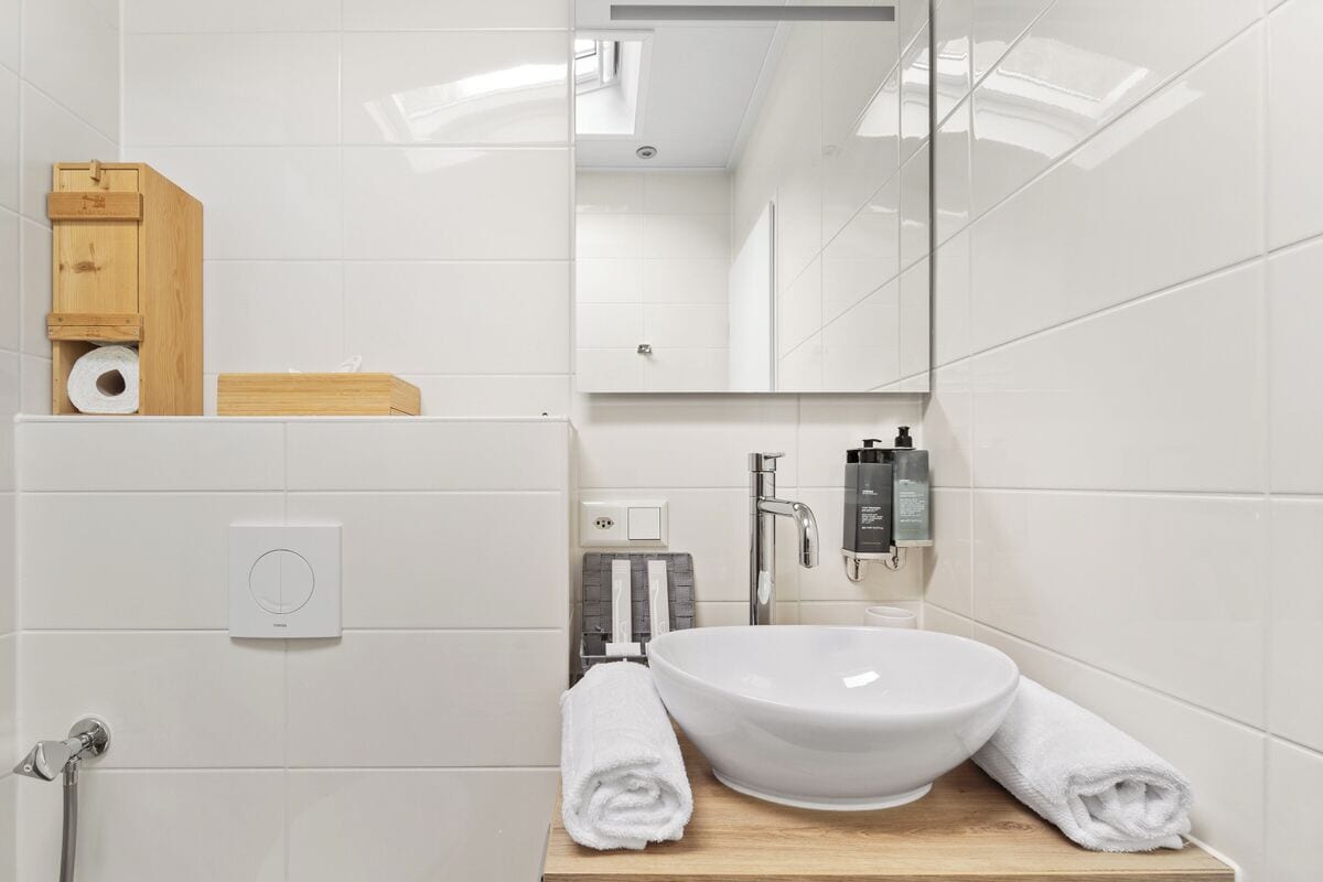 A modern bathroom with a white sink, two towels, a wooden cabinet, and a mirror.