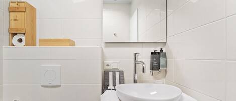 A modern bathroom with a white sink, two towels, a wooden cabinet, and a mirror.