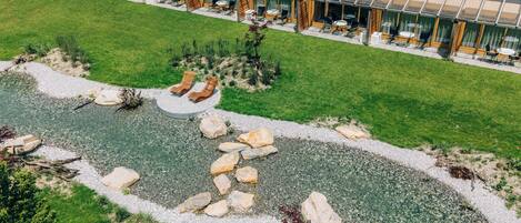 Un edificio moderno con facciata in vetro, area salotto esterna e giardino curato con un piccolo stagno e rocce.