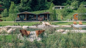 A lakeside cabin with a wooden deck, a small pond, and a forested backdrop.