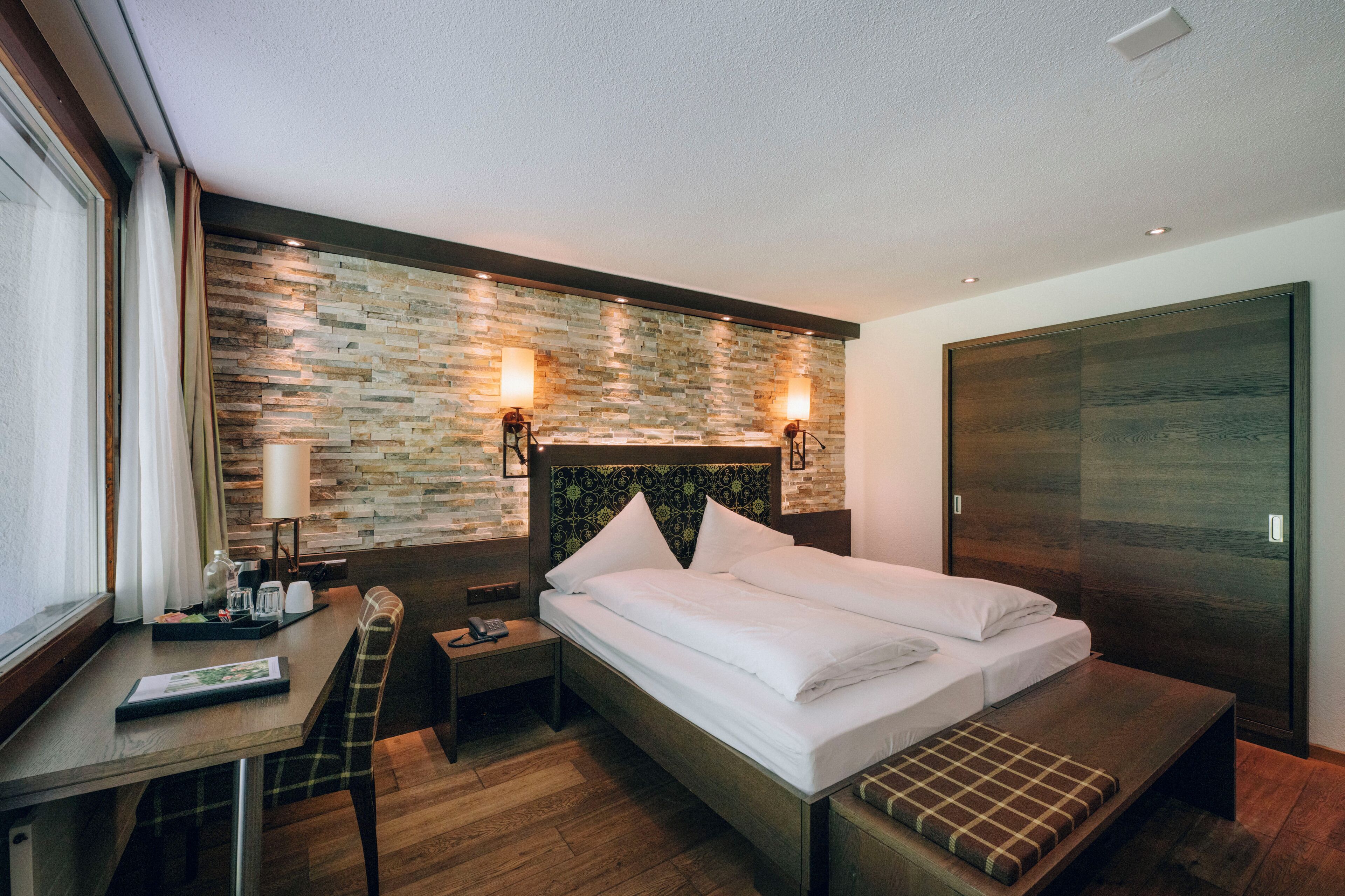 Una habitación de hotel moderna con una cama grande, un escritorio con una silla, una mesita de noche y un banco de madera.