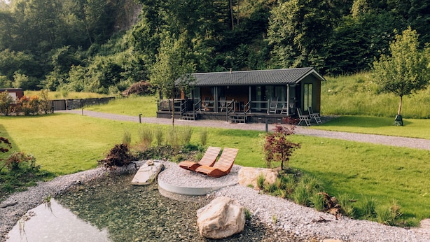 A cabin with a deck, surrounded by a pond and greenery.