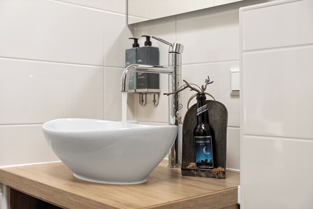 A modern bathroom with a white sink, chrome faucet, and a bottle of Leermond beer on the countertop.