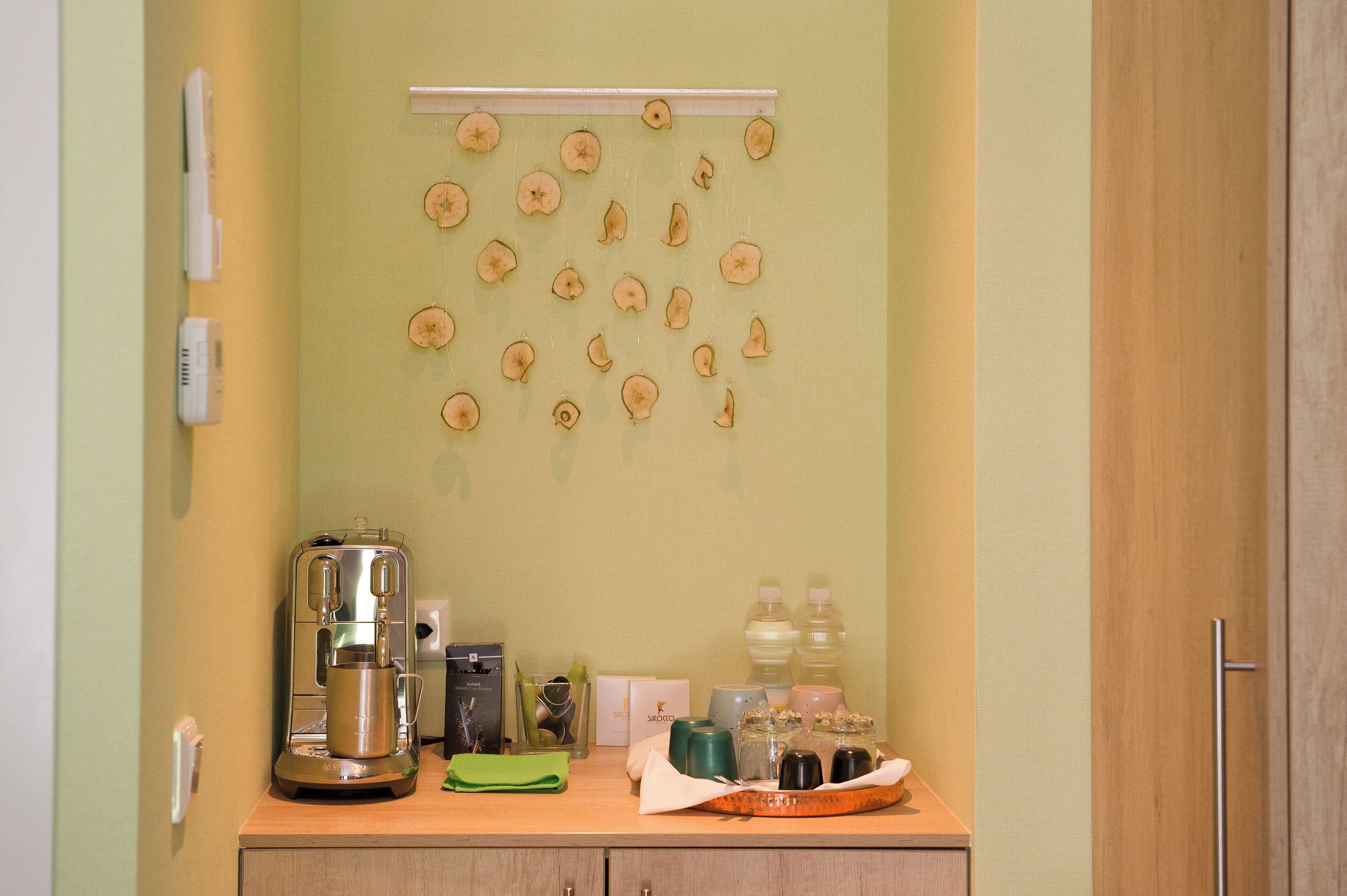 Une petite cuisine équipée d’une machine à café, d’un étendoir mural et de divers articles de toilette disposés sur le comptoir.