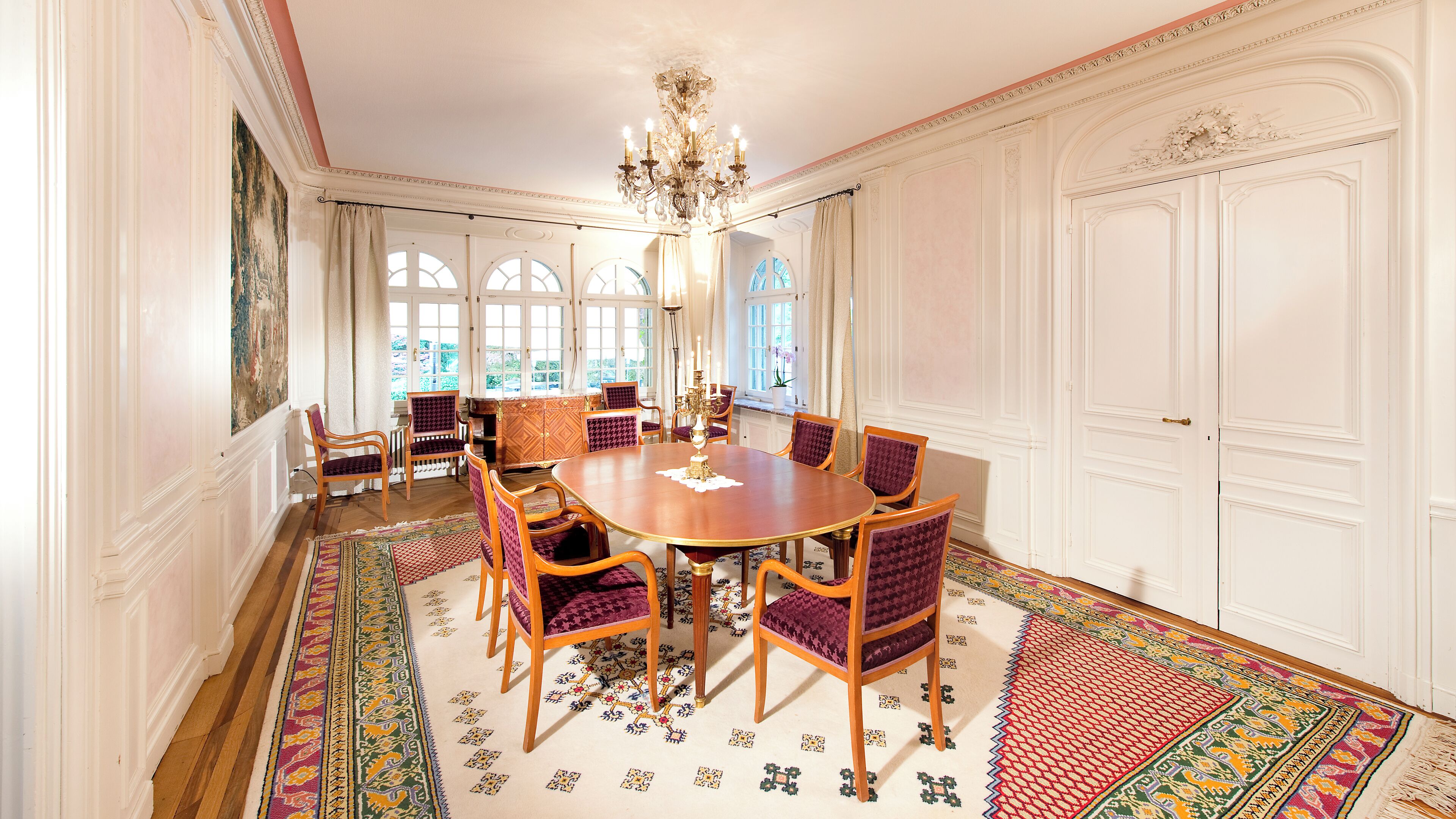 A formal dining room with a large wooden table, six chairs, and a chandelier.