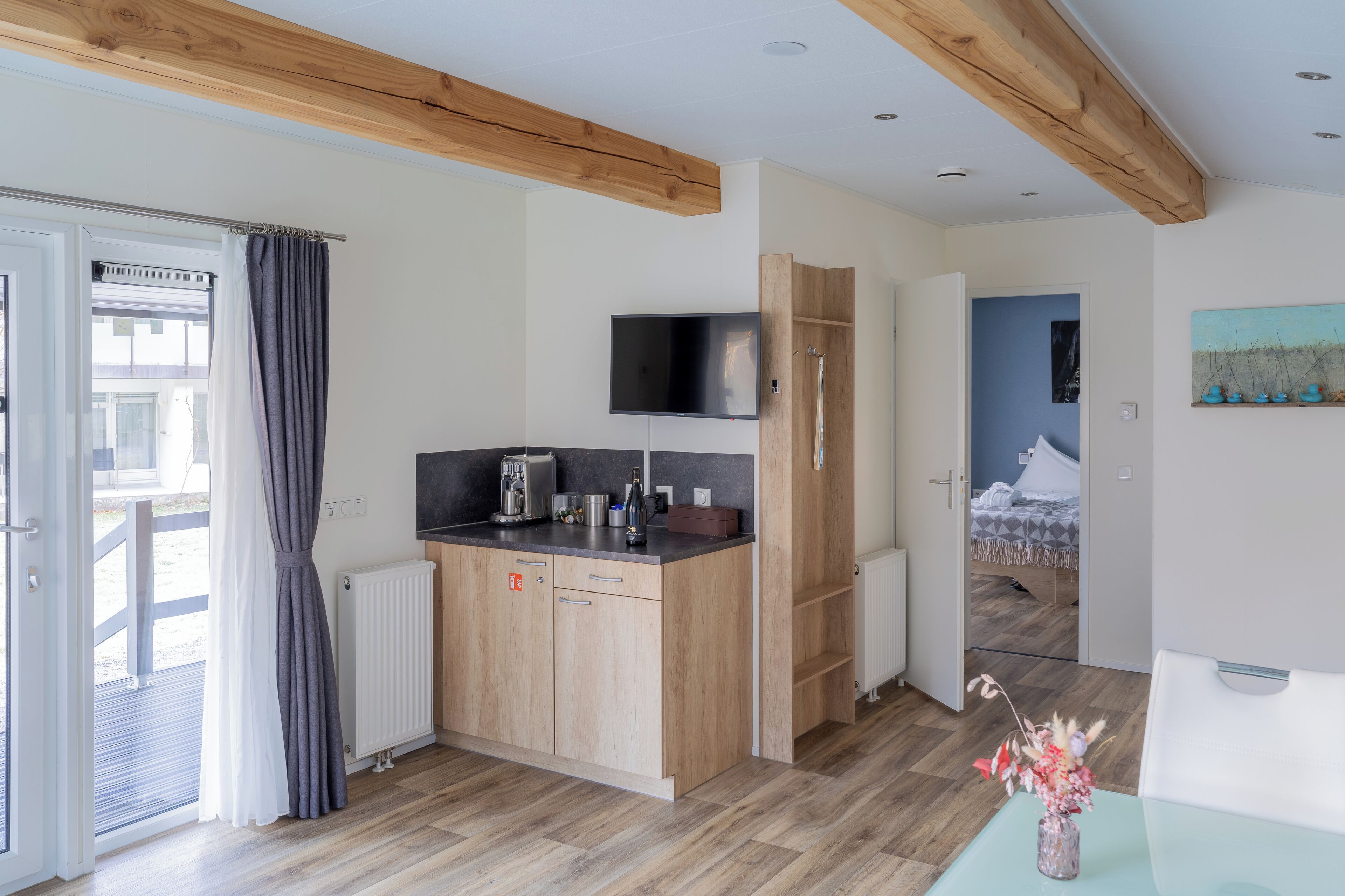 A modern kitchen with wooden cabinets, a built-in TV, and a dining area with a table and vase.