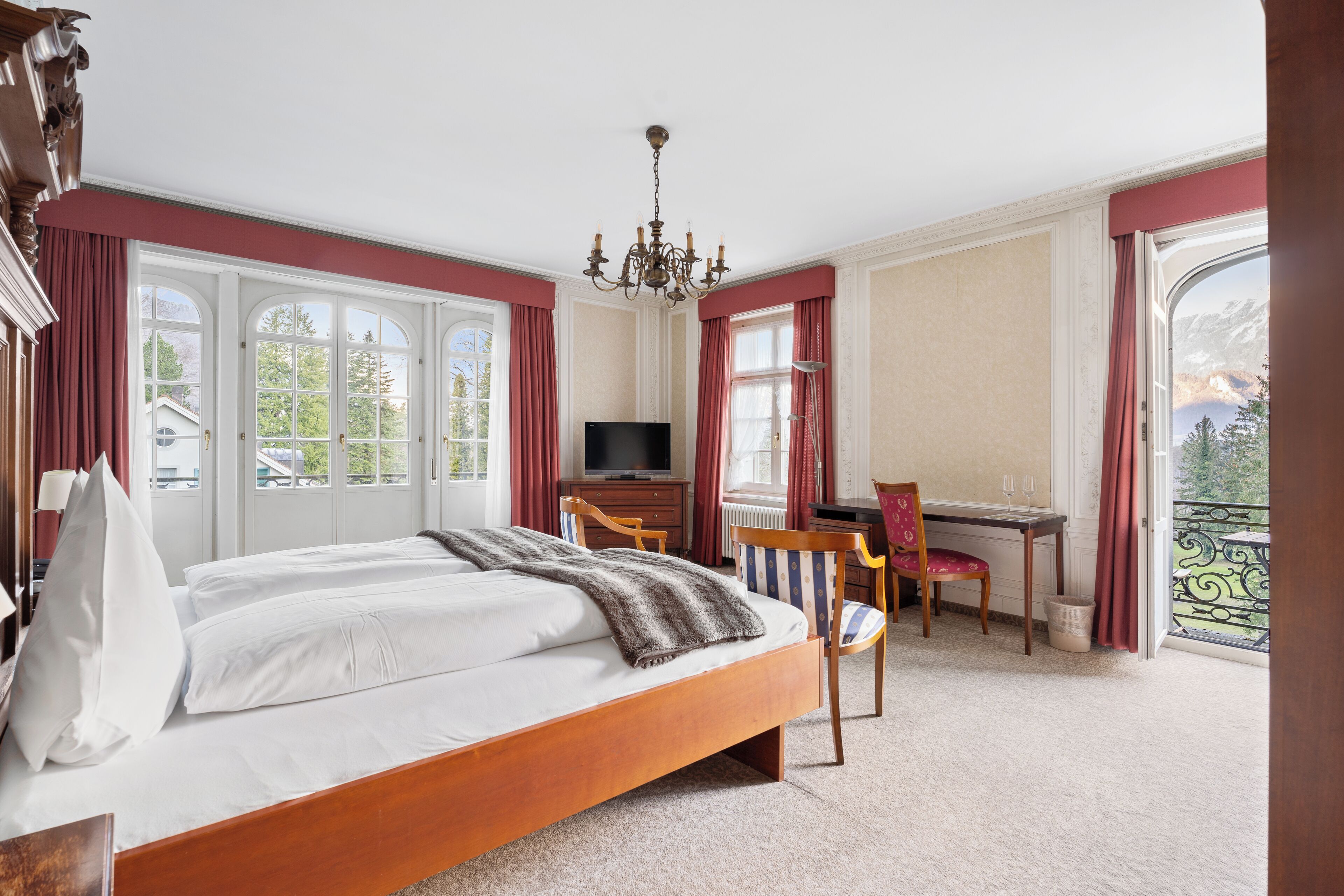 A bedroom with a bed, a desk, a chair, and a TV.