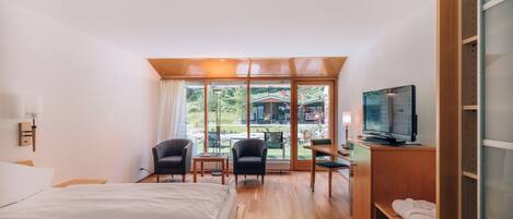 A hotel room with a bed, a desk, a chair, a television, and a view of the outdoors.