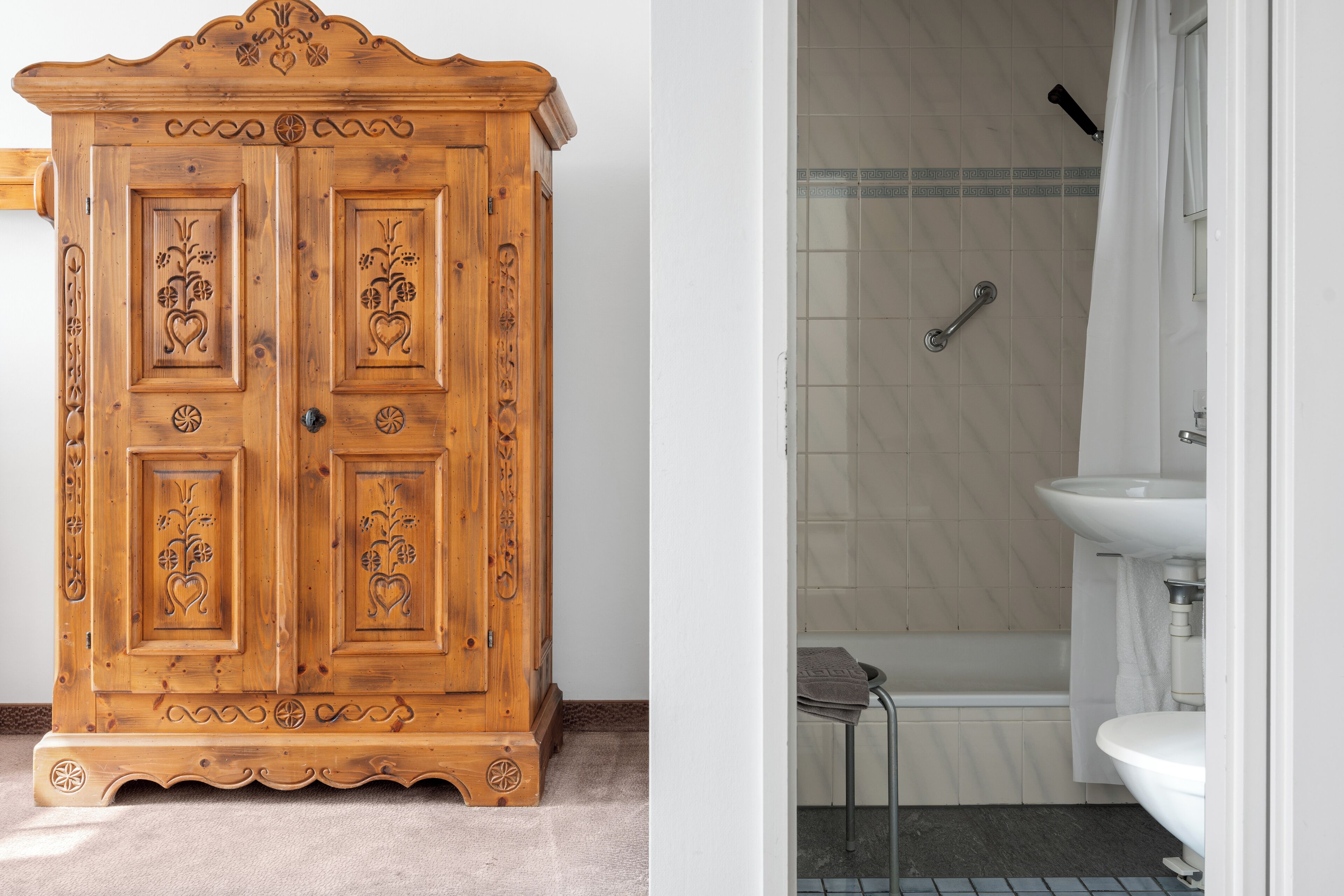 A wooden cabinet with intricate carvings and a bathroom with a bathtub, sink, and shower.