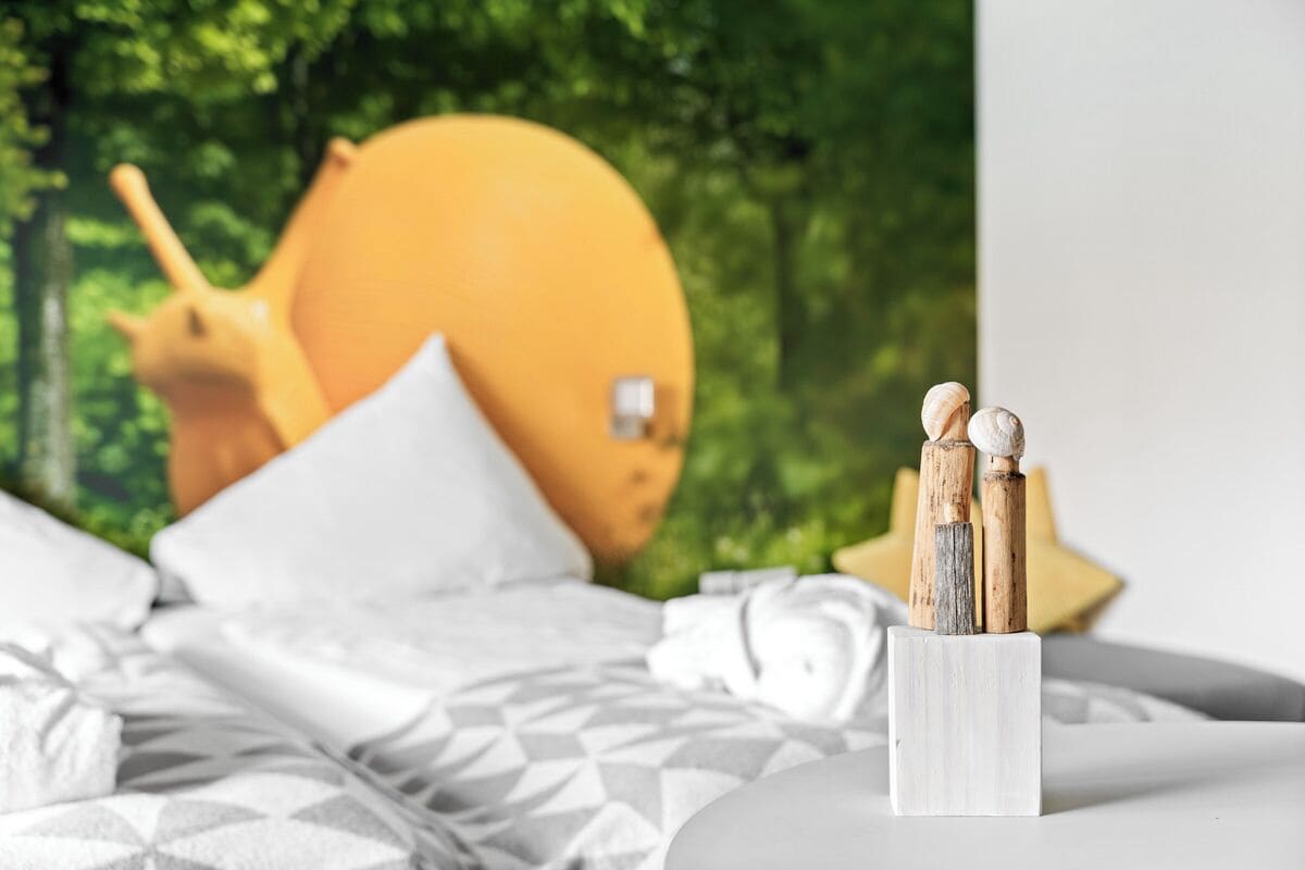 A bed with a geometric patterned bedspread, a white pillow, and a white bedside table with a wooden object on it.