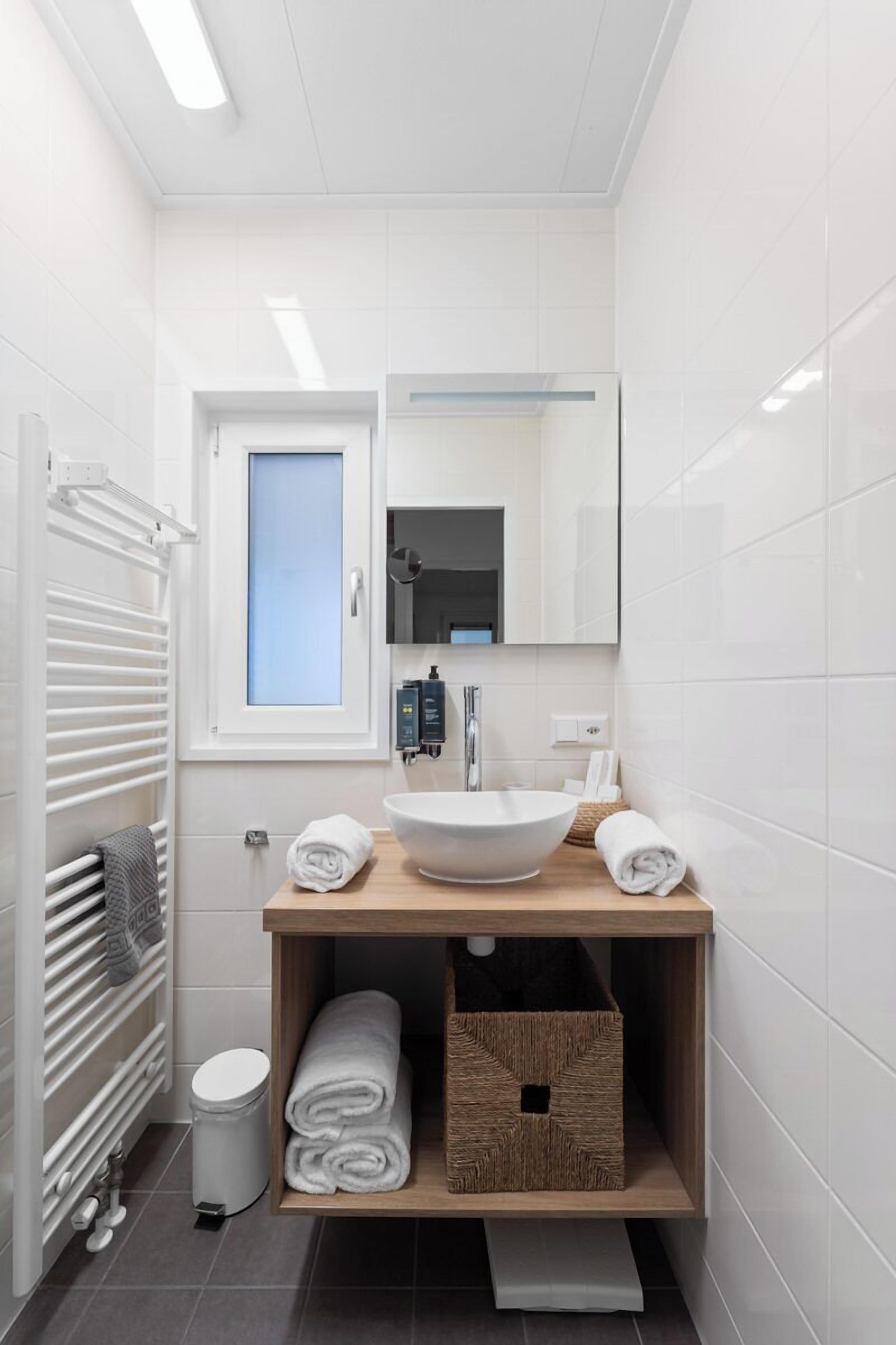 Une salle de bain moderne avec un lavabo blanc, un miroir et un espace de rangement pour les serviettes.