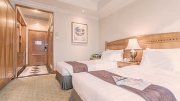A hotel room with two beds, a wooden headboard, a nightstand with a lamp, and a framed picture on the wall.