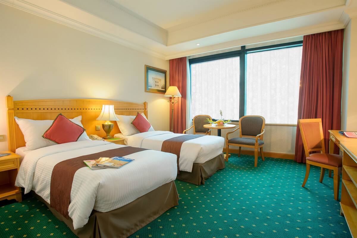 Habitación de hotel con dos camas, un escritorio, una silla, una mesa y una ventana con cortinas.