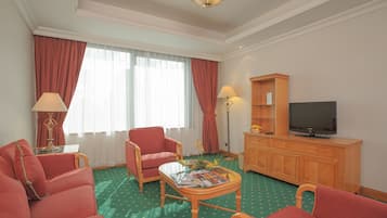 A hotel room with a green carpet, two red sofas, a wooden cabinet with a television, and a floor lamp.