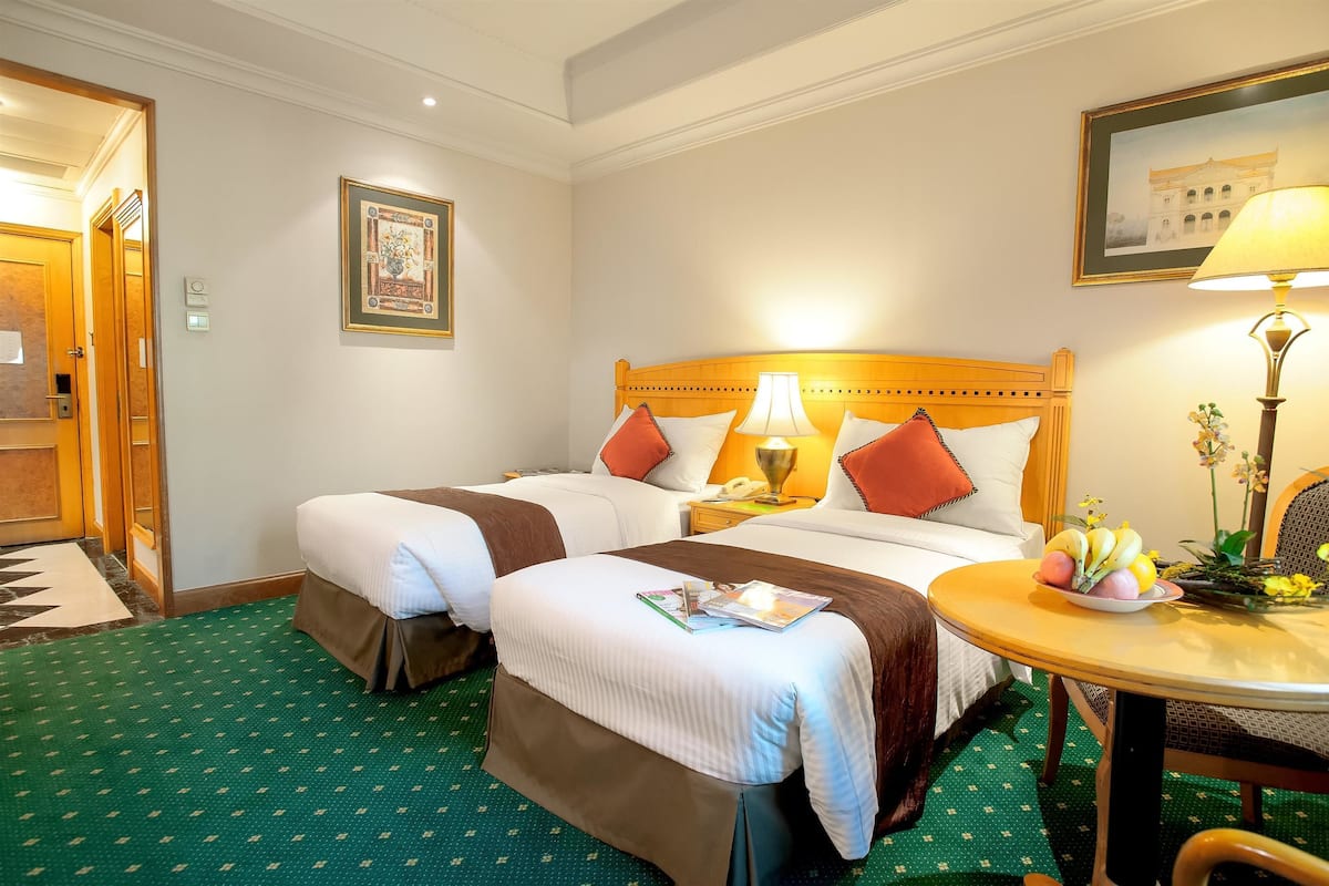 Habitación de hotel con dos camas, una mesa redonda con lámpara y un cuadro en la pared.