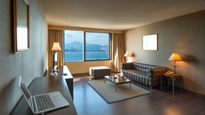 A hotel room with a desk, laptop, sofa, and a view of the city.