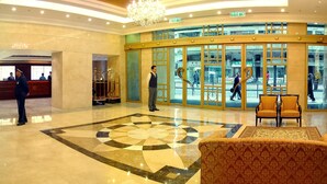 A hotel lobby with a reception desk, a large chandelier, and a patterned floor design.