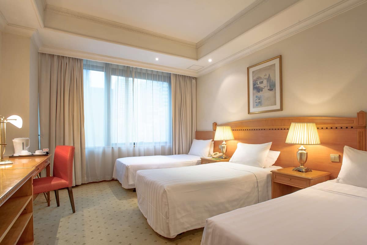 Habitación de hotel con dos camas, un escritorio, una silla y un ventanal con cortinas.