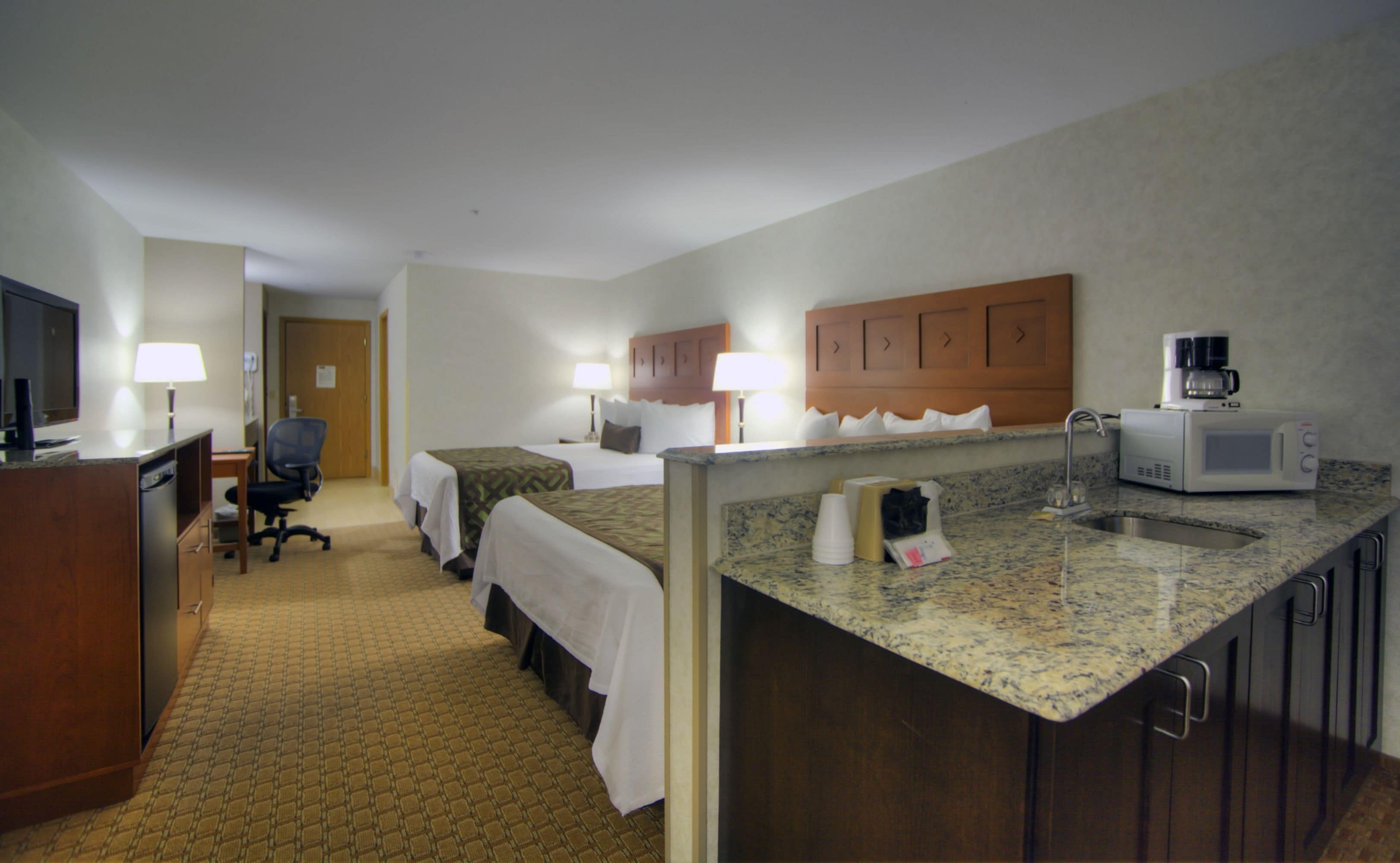 A hotel room with two beds, a desk, a television, a microwave, and a sink.