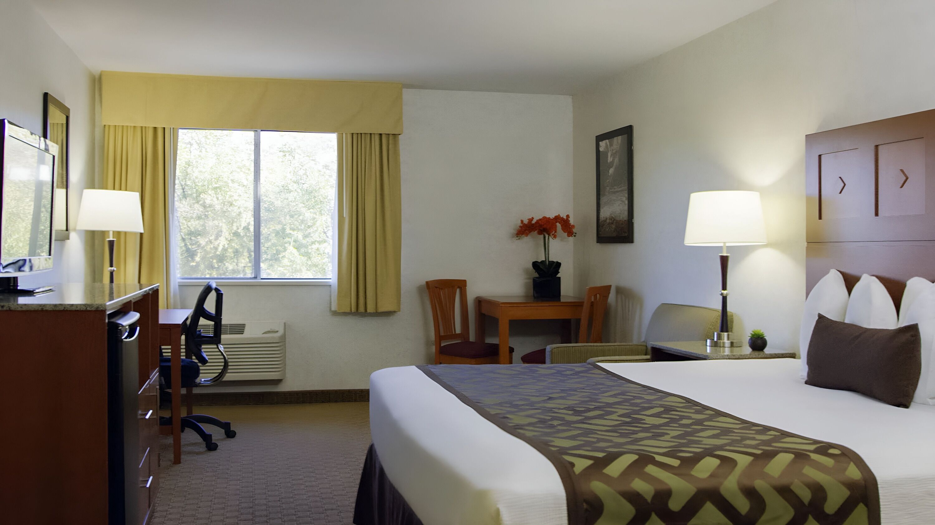 A hotel room with a bed, desk, chair, and a window with curtains.