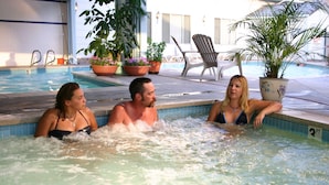 Une zone autour d’une piscine où se trouvent trois personnes dans l’eau, le tout agrémenté de plantes en pot et de chaises longues.